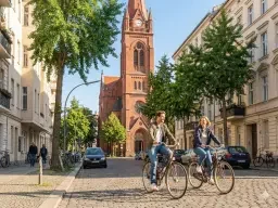 Ein Paar fährt mit dem Fahrrad an der Kirche zum Heilsbronnen nahe der Praxis für Paartherapie in Berlin Schöneberg vorbei